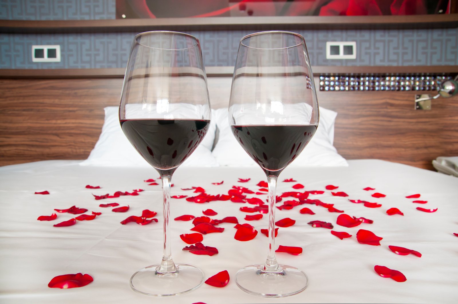 Two glasses of wine side by side on top of hotel bed