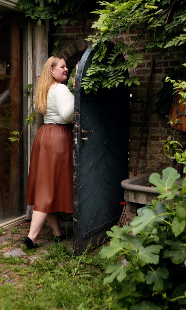 a woman in a brown skirt and a white shirt standing next to a door smiling